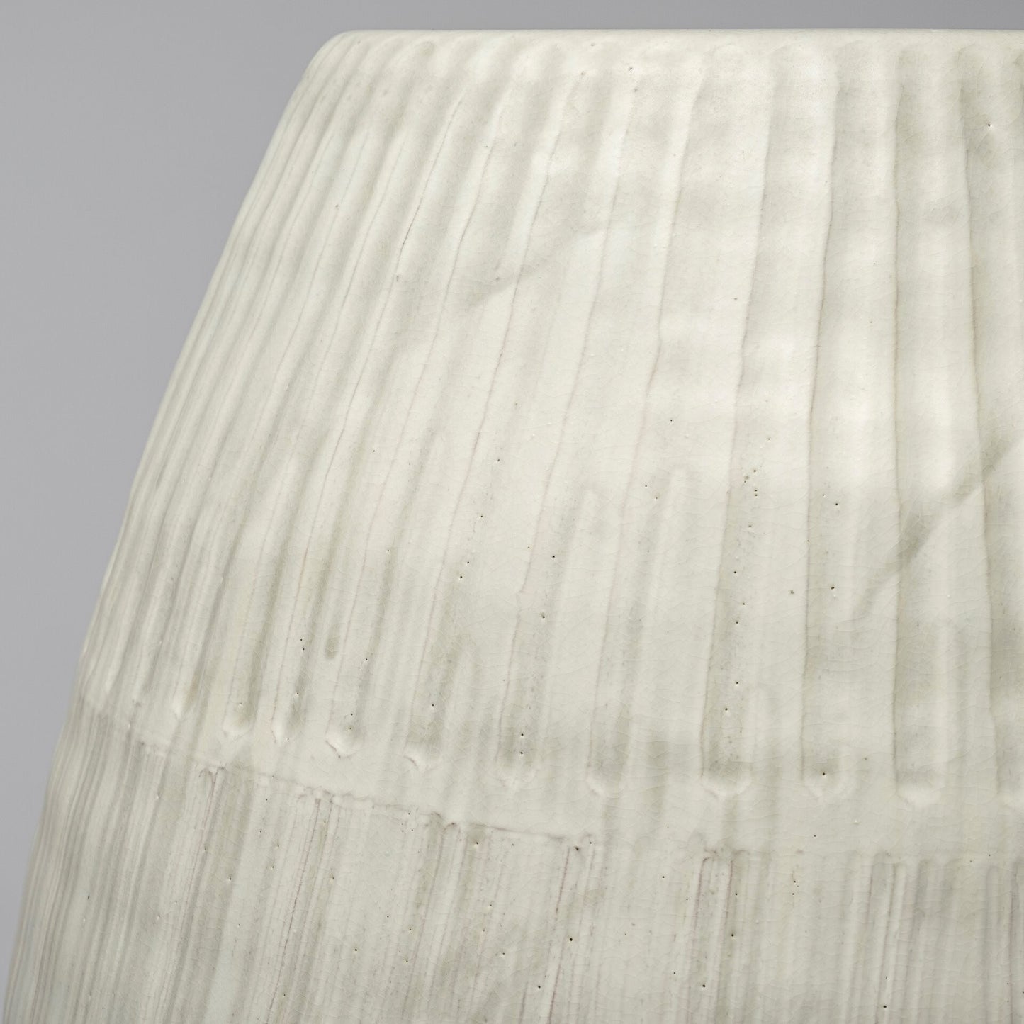 Close-up of a textured white ceramic vase against a gray background