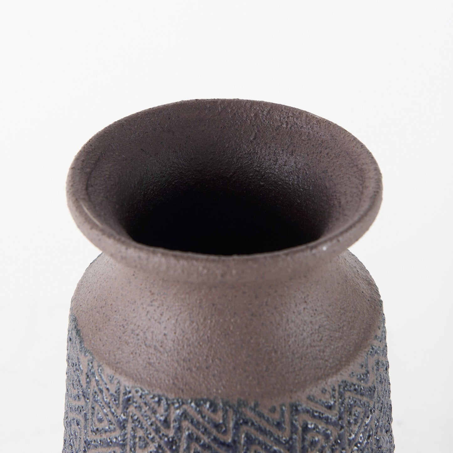 Detailed shot of handcrafted ceramic vase highlighting textured brown finish and intricate black tribal geometric embossing