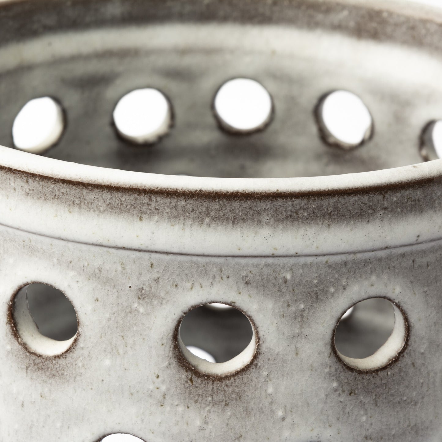 Detail shot of pierced dot pattern on white ceramic vase showing how light filters through circular perforations, creating dimensional visual interest