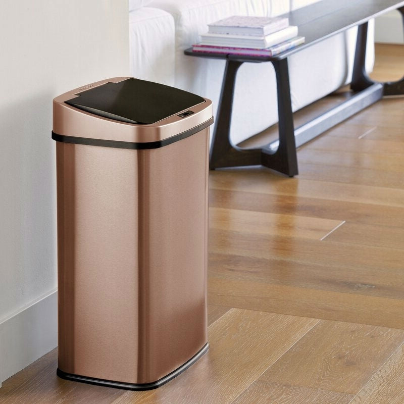 Gold copper motion sensor trash can in modern kitchen interior with wooden cabinets