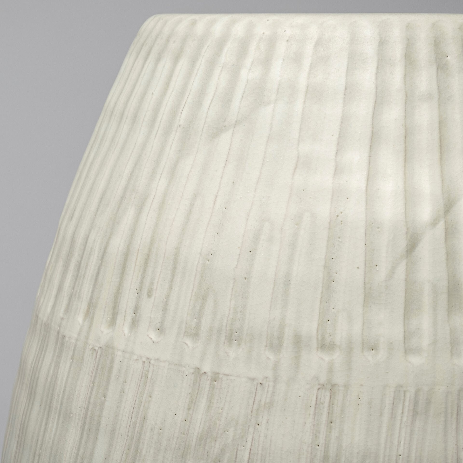 Close-up of a textured white ceramic vase against a gray background