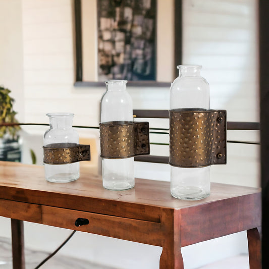 Set of three clear and bronze hammered cylinder metal and glass table vases showing industrial modern design perfect for contemporary home decor
