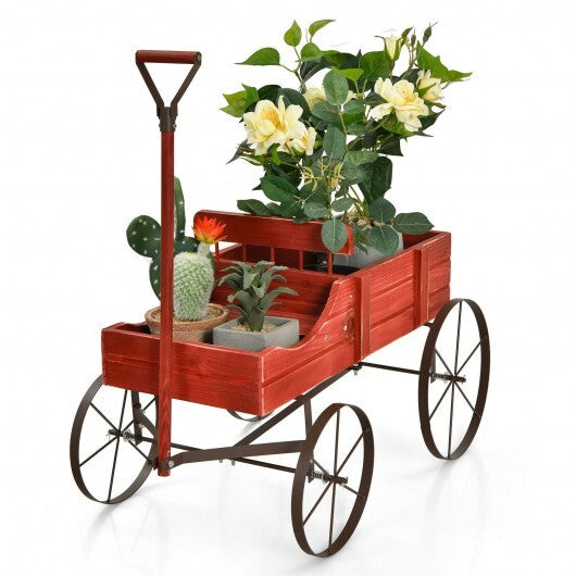 Red wooden wagon planter with wheels and handle filled with green flowering plants
